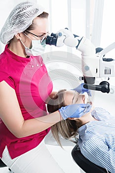 A female professional dentist examines a female patient with a stamotologic microscope in her office. Stamotologist