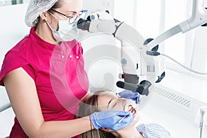 A female professional dentist examines a female patient with a stamotologic microscope in her office. Stamotologist