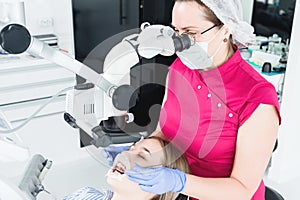 A female professional dentist examines a female patient with a stamotologic microscope in her office. Stamotologist