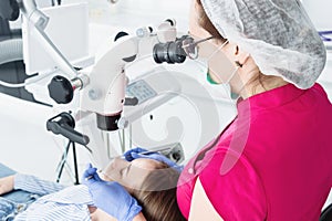 A female professional dentist examines a female patient with a stamotologic microscope in her office. Stamotologist