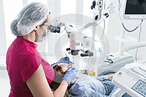 A female professional dentist examines a female patient with a stamotologic microscope in her office. Stamotologist