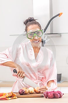 Female protects herself from onion cutting smell by a snorchel while standing in the kitchen dressed in silk nightgown