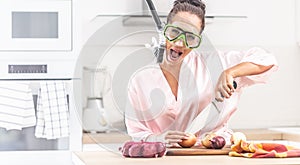 Female protects herself from onion cutting smell by a snorchel while standing in the kitchen dressed in silk nightgown