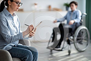Female psychologist working with handicapped adolescent in wheelchair at office, copy space