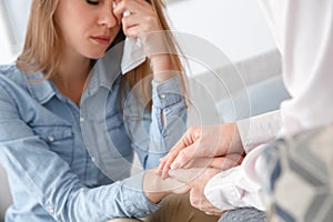 Female psychologyst therapy session with client indoors sitting girl wiping tears away close-up