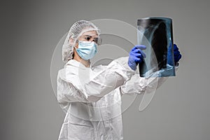 Female pulmonologist or oncologist holding chest X-ray scan,inspecting COVID-19 patient lungs,wearing PPE uniform. Coronavirus