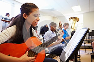 Female Pupil Playing Guitar In High School Orchestra