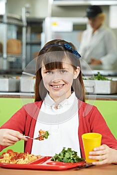Female Pupil Sitting At Table In School Cafeteria Eating Healthy