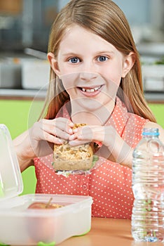 Female Pupil Sitting At Table In School Cafeteria Eating Healthy