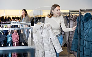 Female purchaser choosing winter down jacket in shopping center