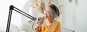 Female radio host streaming podcast using microphone and laptop at his home studio. Wide image