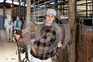 Female rancher carrying horse tack and saddle in horse farm