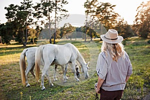 Female rancher with hat looking at white horses on pasture