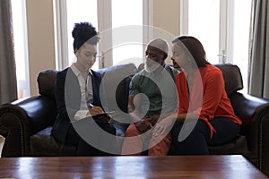 Female real estate agent and senior couple discussing over clipboard in living room