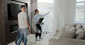 Female real-estate agent showing family spaceous house. Young couple entering modern apartment they are going to buy