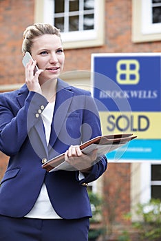 Female Realtor On Phone Outside Residential Property For Sale