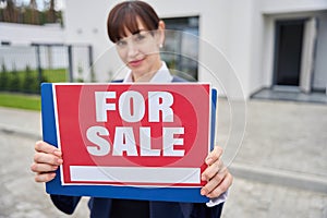 Female realtor stands with a for sale sign