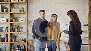 Female realtor in suit is showing loft style flat to young man and woman looking for new apartment. Buyers are excited