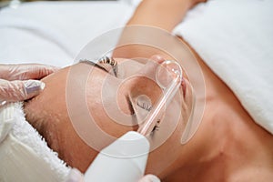 Female receiving galvanic facial treatment in spa cosmetologist wearing gloves professional services photo
