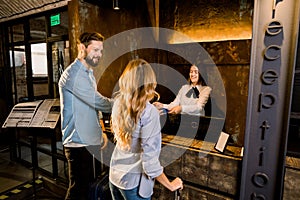 Female receptionist and young couple in hotel. Happy Couple, Caucasian man and woman, Checking In At Hotel Reception