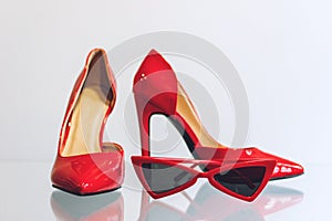 Female red fashion accessories. Red women heel shoes and trendy red cat eye sunglasses on the shelf in the store shop. Set of