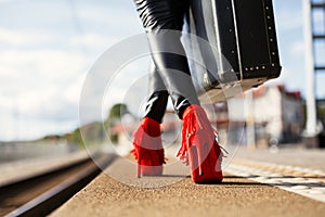 Female with red high heels and suitcase in train station