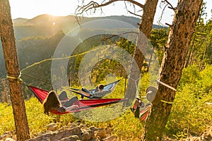 Female in a red and a man in a blue hammock enjoying the sunset on the slope of a mountain