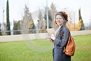 Female redhead student carrying notebook and coffee to go