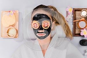 Female relaxing with charcoal facial mask in spa resort.