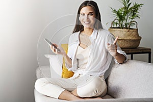 Female relaxing at home, using smartphone to text messages, check email, looking at the camera with showing success..