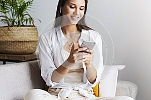 Female relaxing at home, using smartphone to text messages, share photos, communicate with friends, check email.