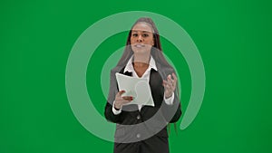 Female reporter isolated on chroma key green screen background. African American woman news host in suit reads paper