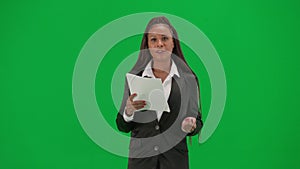 Female reporter isolated on chroma key green screen background. African American woman news host in suit reads paper