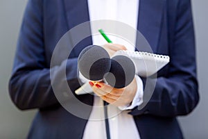 Female journalist at news conference or media event, writing notes, holding microphone