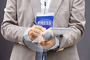 Female journalist at news conference or media event, writing notes, holding microphone