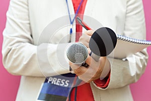 Female reporter at press conference, writing notes, holding microphone