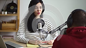 Female reporter talking to media person and sitting at table during radio broadcast in studio spbd.