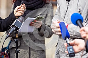 News reporter or TV journalist at press conference, holding microphone and writing notes