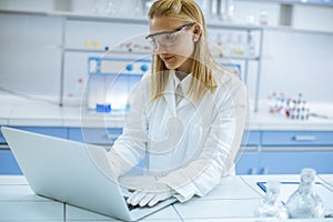 Žena výskumník v biely laboratórium srsť a ochranný ochranné okuliare prenosný počítač zatiaľ čo pracovné v laboratórium 