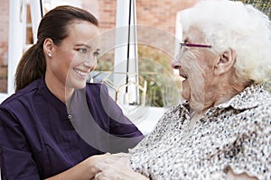 Female Resident Sitting In Chair And Talking With Carer In Retirement Home