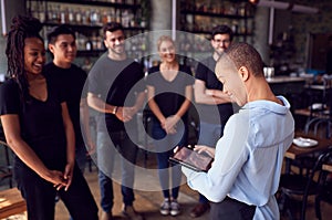 Female Restaurant Manager With Digital Tablet Giving Team Talk To Waiting Staff