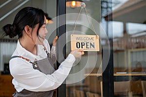 A female restaurant staff or small business owner is hanging an open sign on the entrance door