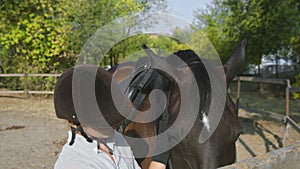 Female rider in riding clothes and helmet stroking her horse and looks at the camera