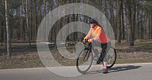 Female on road bike, portrait. Woman standing with bicycle in forest on empty road. Cyclist athlete in helmet preparing for cycle