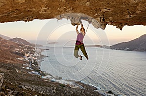 Female rock climber on challenging route in cave at sunset