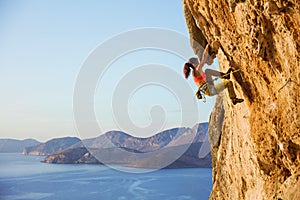 Female rock climber on challenging route on cliff, view of coast photo