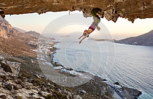 Female rock climber resting while hanging upside down on challenging route in cave at sunset