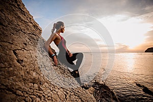 Female rock climber watching sunset over sea