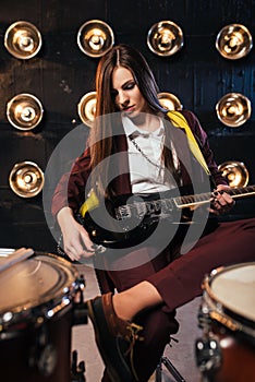 Female rock guitarist sitting behind the drum kit