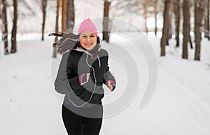 Female runner jogging in cold winter forest wearing warm sporty running clothing and gloves headphones